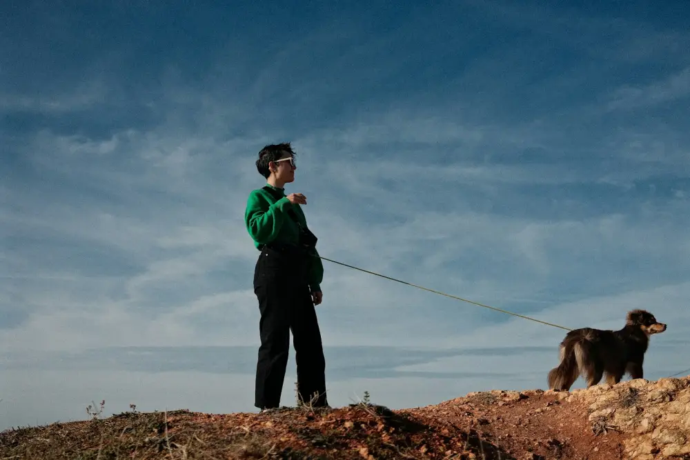 A woman walks her dog under a bright blue sky.